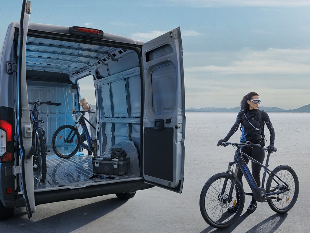 Person with a bicycle near an open van carrying another bicycle.