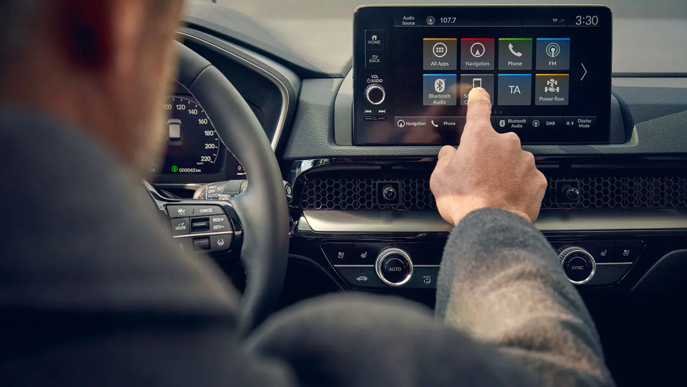 Person using a touch screen in a car's dashboard for navigation and audio control.