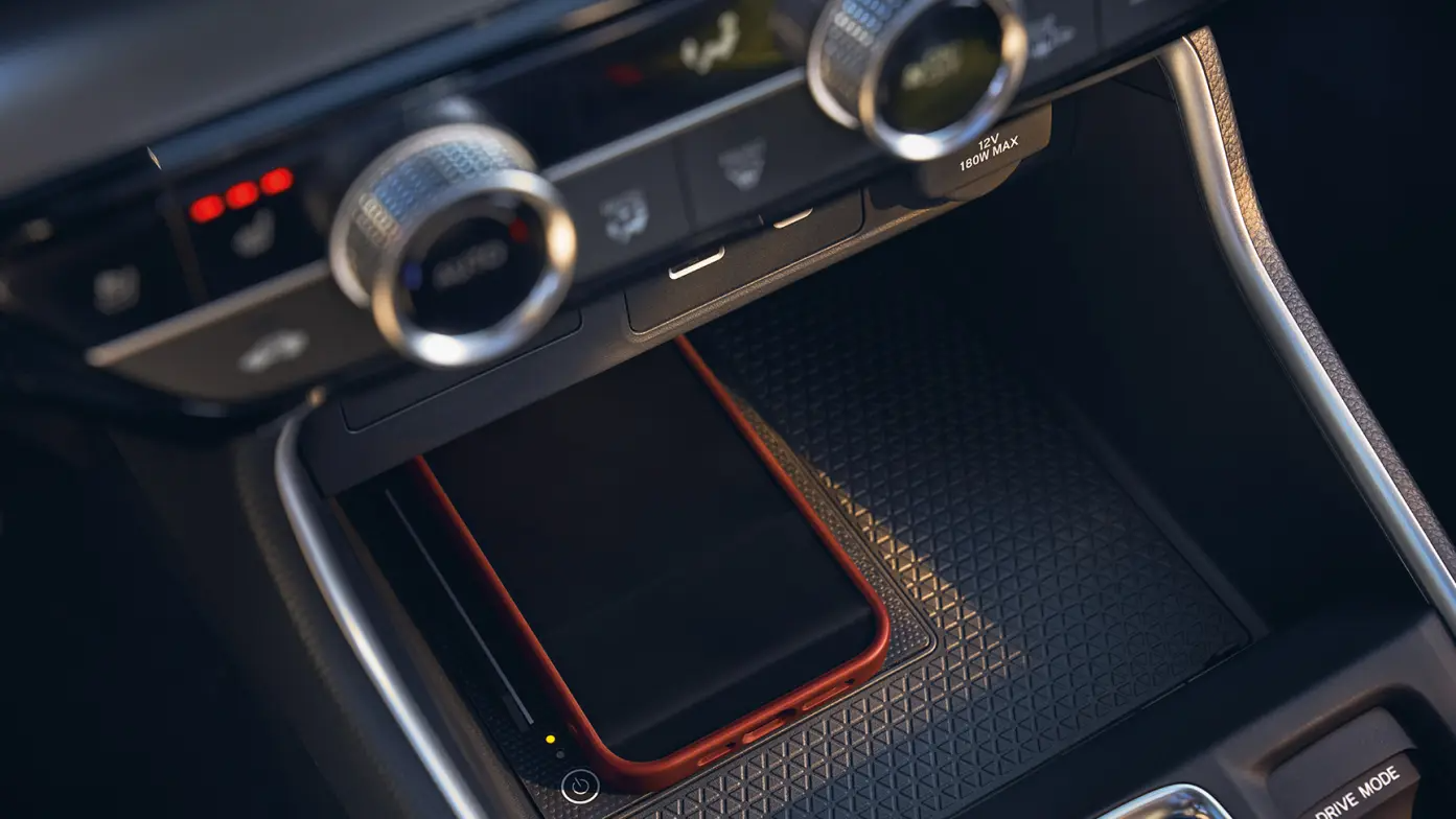 Smartphone with a red case on a car's wireless charging pad.