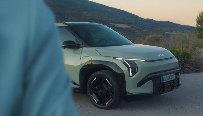 A light green car parked on a road with rolling hills in the distance.