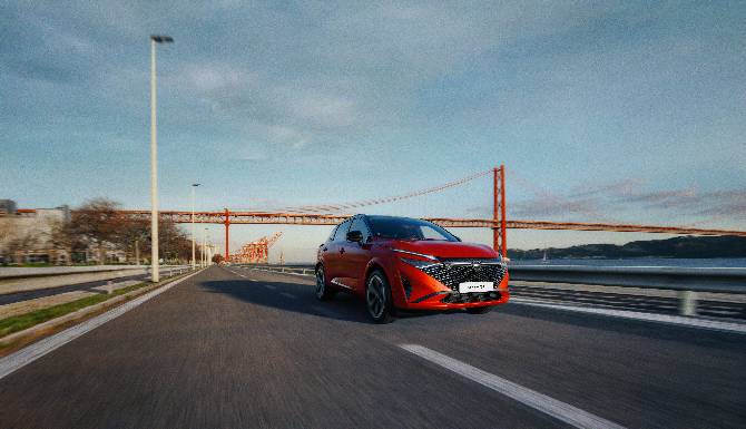 Red car driving on a road near a suspension bridge.