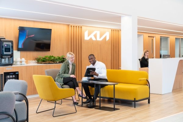 Two people sitting on yellow sofas, looking at a brochure in a modern waiting area.