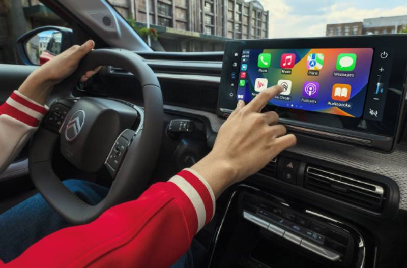 Person using a touchscreen in a car, displaying various app icons.