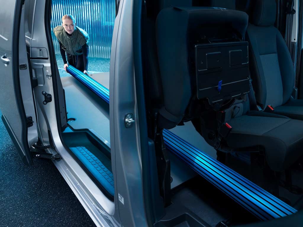 Person loading long blue objects into a van through the side door.