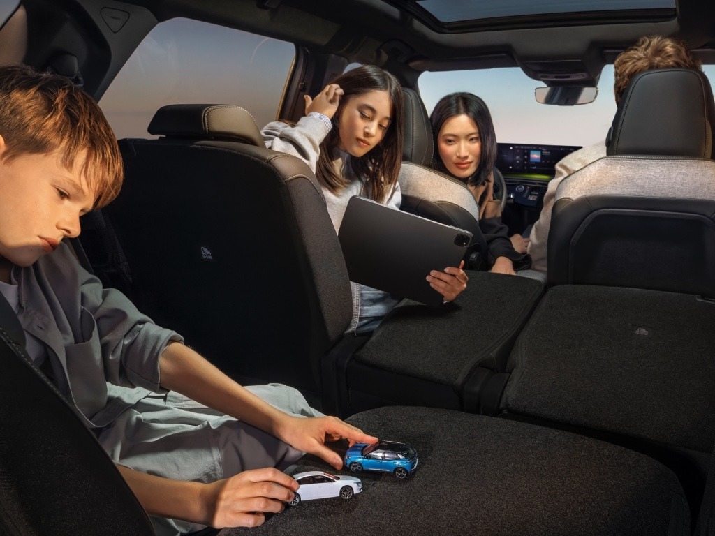 Inside a car, a child plays with toy cars while others look at a tablet.