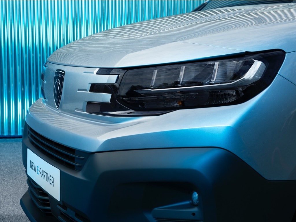 Close-up of a silver car front with a prominent badge and sleek headlights.