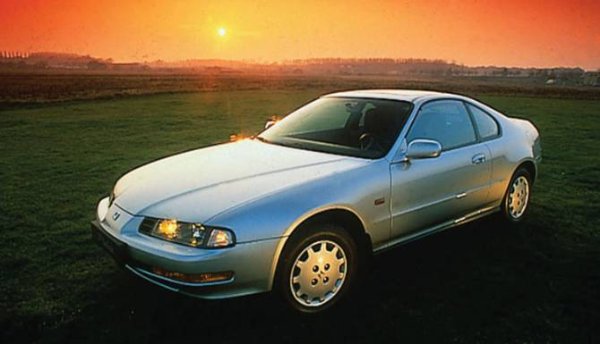 Silver coupe car parked on grass with a sunset in the background.