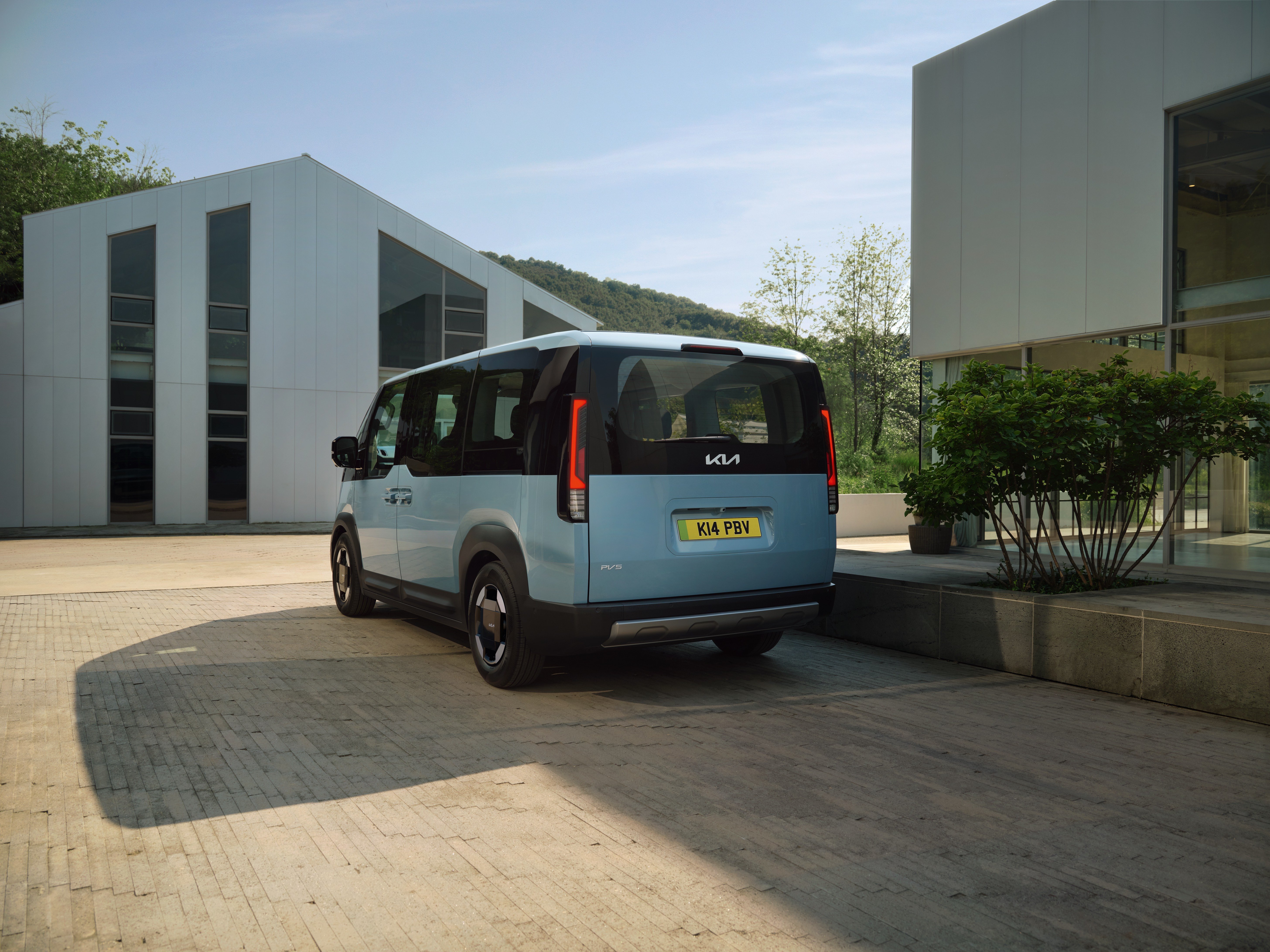 Blue Kia van parked in front of modern buildings.
