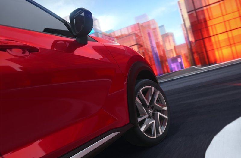 Red car driving past modern buildings on a road.
