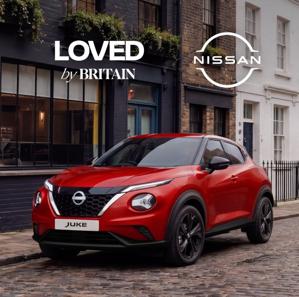 Red Nissan Juke parked on a cobblestone street with branding logos above.