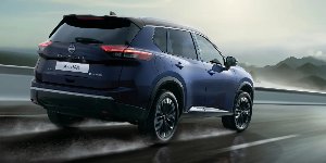 Blue Nissan X-Trail driving on wet road with mountains in the background.