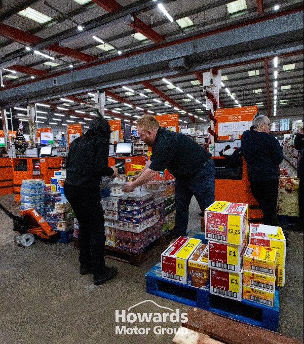 Two people stacking product boxes in a warehouse aisle.