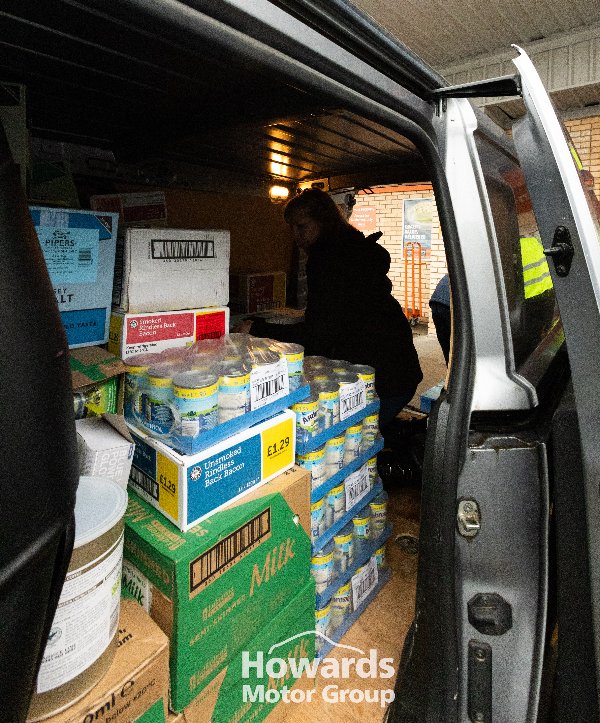 Van loaded with boxes and canned goods, with a person organising the contents inside.