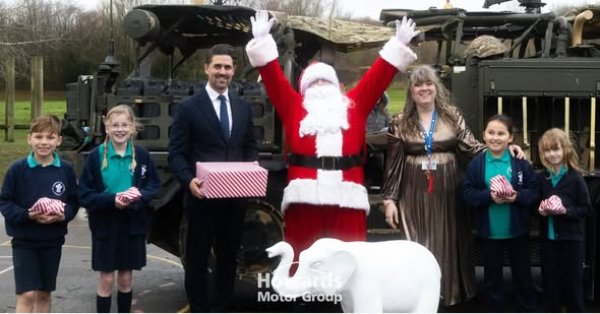 Santa and a group of children with gifts in front of a military vehicle.
