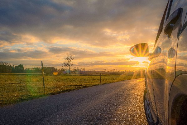 Side view of a car on a road during sunset with fields in the distance.