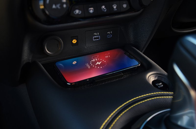 Smartphone charging wirelessly in a car centre console with start button and gear stick visible.