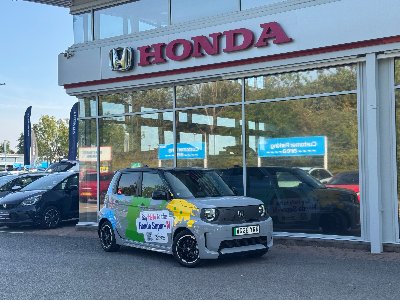Small Honda car parked outside a dealership with promotional graphics on the side.