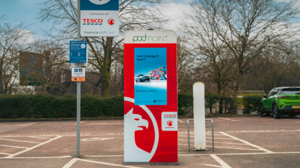 Pod Point EV charging kiosk at Tesco car park, displaying Vauxhall Corsa ad.