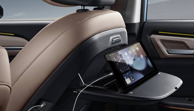 Tablet attached to car seat back with folding tray and USB cable.