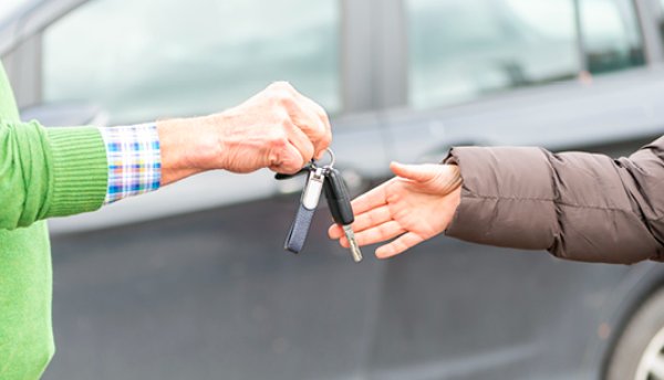 Two people exchanging car keys in front of a vehicle.