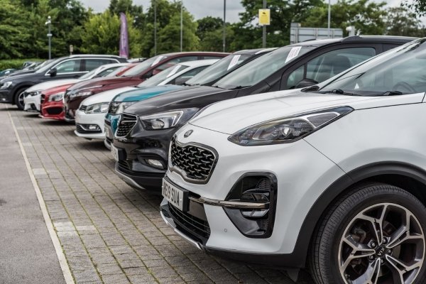 Row of parked cars in a dealership forecourt.