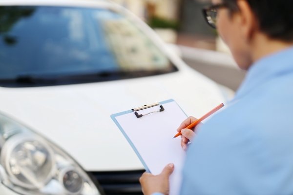 Person standing by a car, writing on a clipboard.