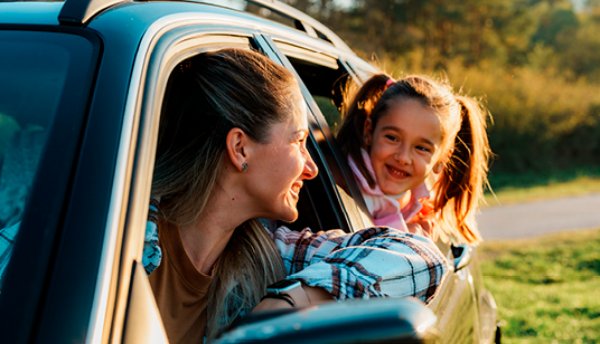 Woman and child smiling, looking out of car windows in daylight.