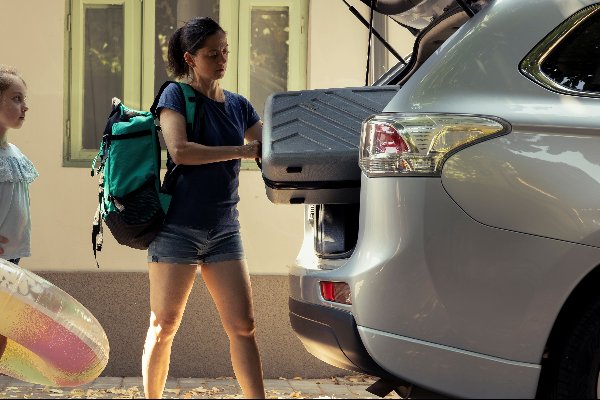 Woman packing car boot with girl holding inflatable ring.
