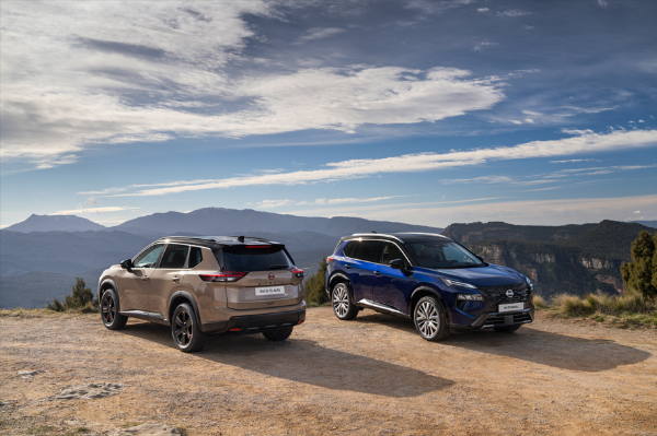 Two Nissan X-Trail cars parked on a hill with mountains in the background.